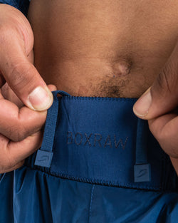Man in a navy sauna suit tracksuit with a white boxraw logo on the chest as well as adjustable wrist straps and made from polyester.